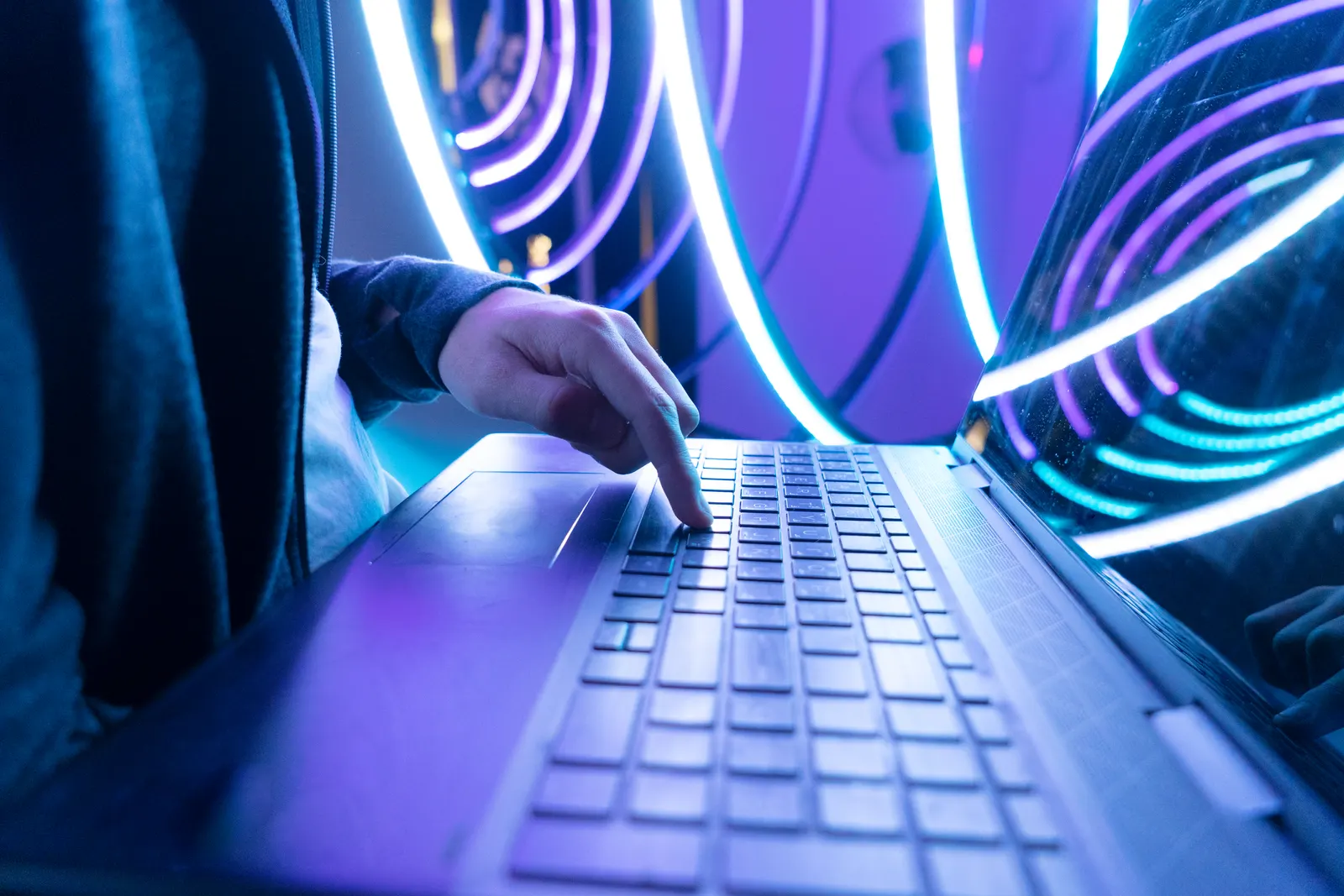 Manos escribiendo código en un portátil bajo luces de neón